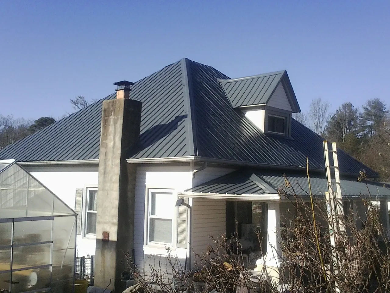 Dark blue standing seam metal roof on a white farmhouse with dormer — Slate & Tile Roof Repair by Roofing Brothers in Apple Valley