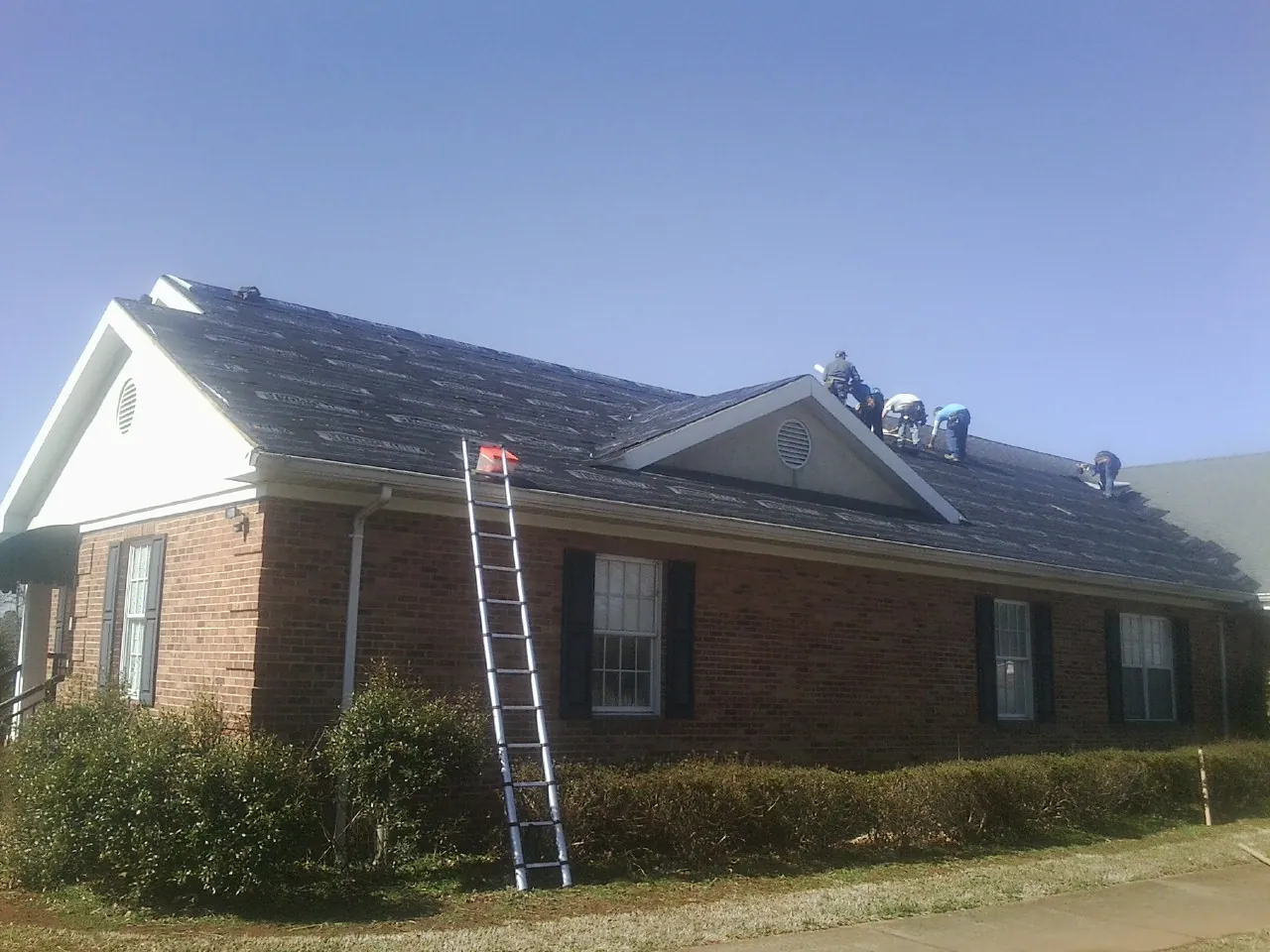 Crew tearing shingles off a brick ranch roof with a ladder set — Emergency Roof Repair work by our crew in Apple Valley