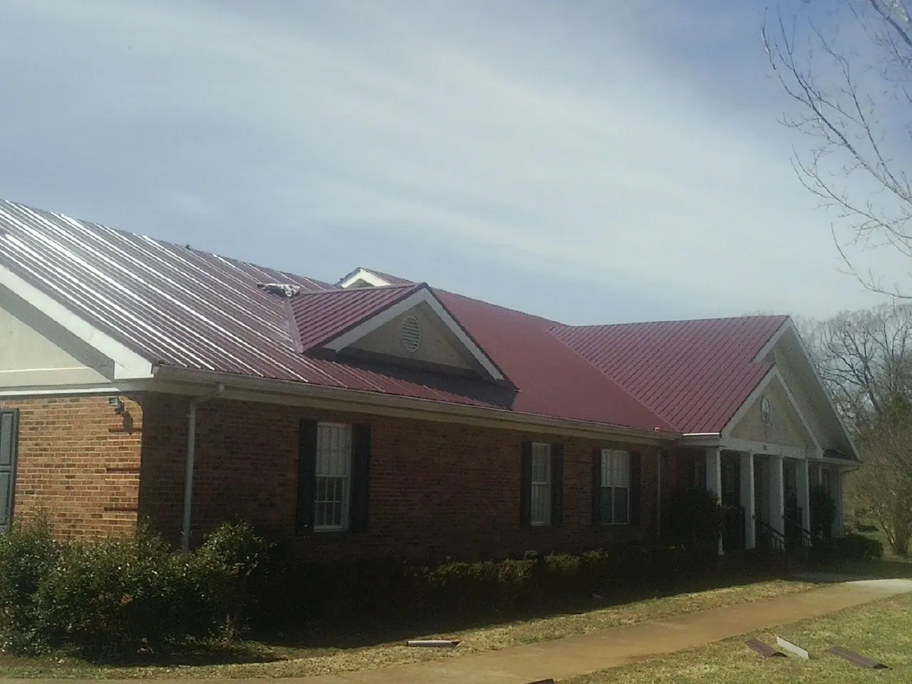 Red metal roof with gabled entries on a long brick building, from a Hail Damage Roof Repair job in Apple Valley