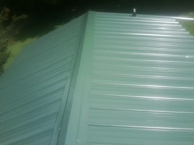 New green metal panels meeting at the ridge of a roof — Flat Roof Repair work by our crew in Apple Valley