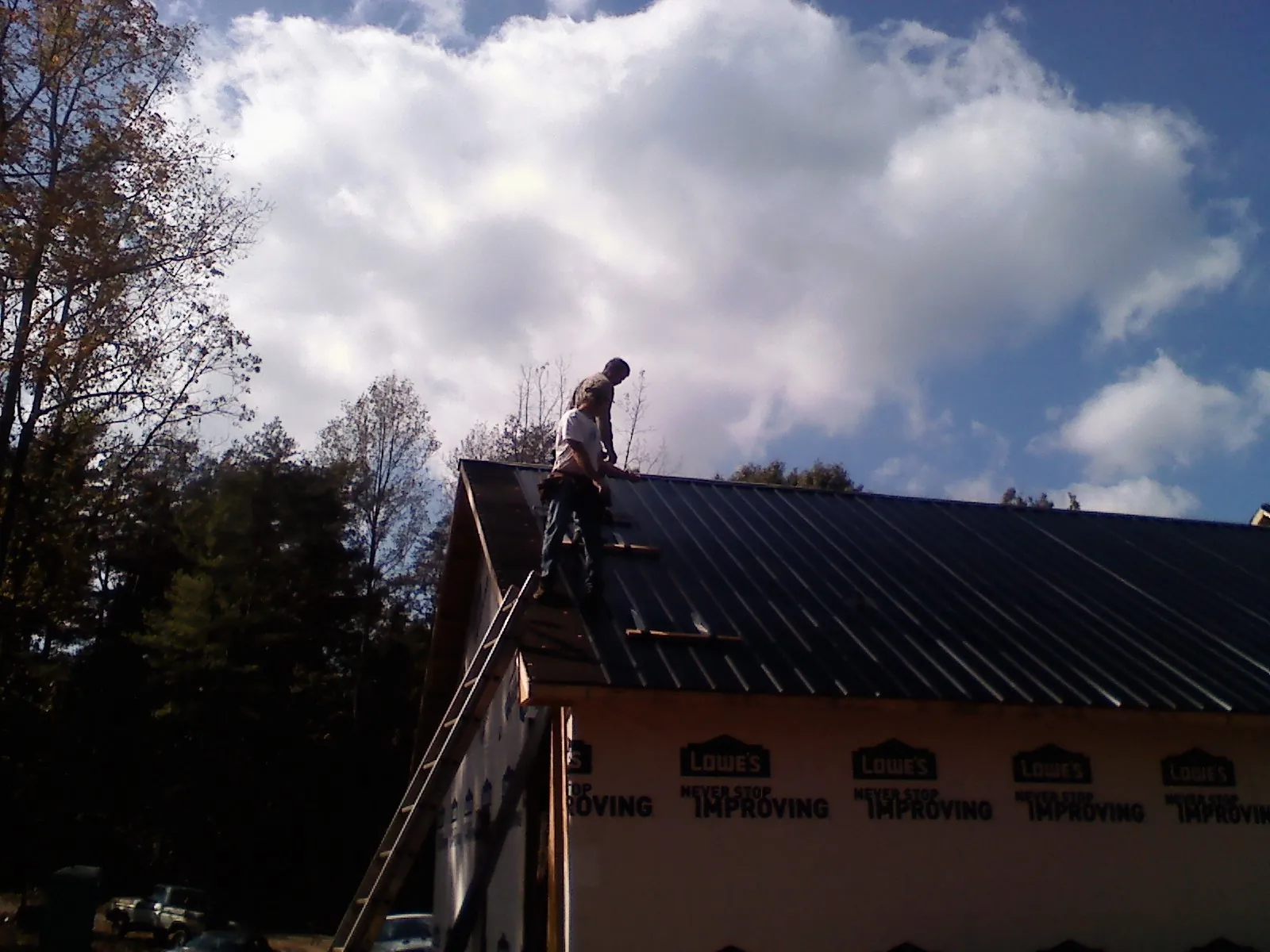 Roofer fastening dark metal panels high against a cloudy sky, from a Roof Inspection job in Apple Valley