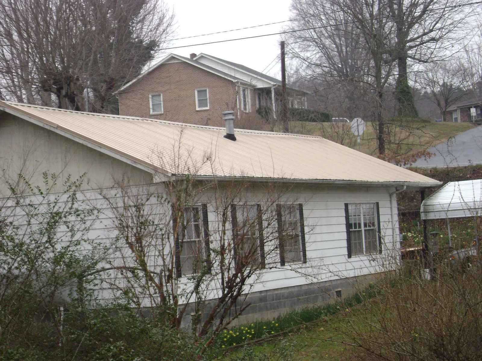 Tan metal roof on a white sided house set into a hillside — Commercial Roofing by Roofing Brothers in Apple Valley